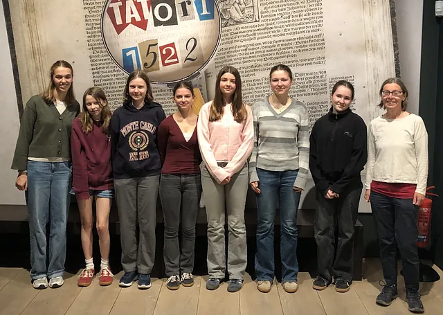 Eine Gruppe Jugendlicher mit Pastorin Nicola Nehmzow vor einer Fotowand zum Thema Buchdruck in Wittenberg.