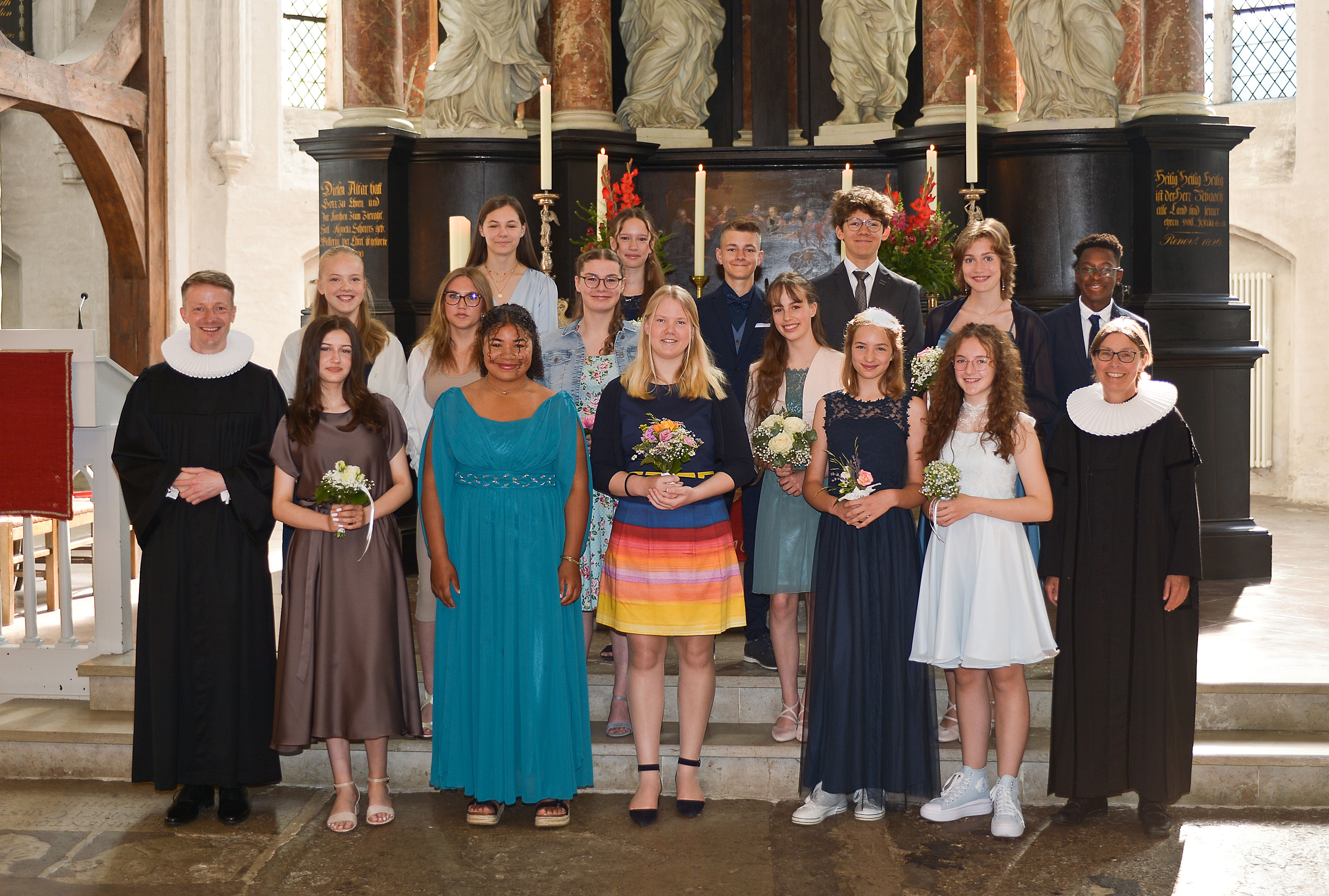 Ein Gruppenfoto von Konfirmanden vor dem Altar in St. Aegidien, umrahmt von Pastorin Nicola Nehmzow und dem damaligen Vikar Tobias Knöller